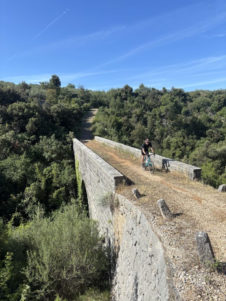 Cyclist riding across a stone bridge on Brač Island during a Croatia gravel cycling tour.